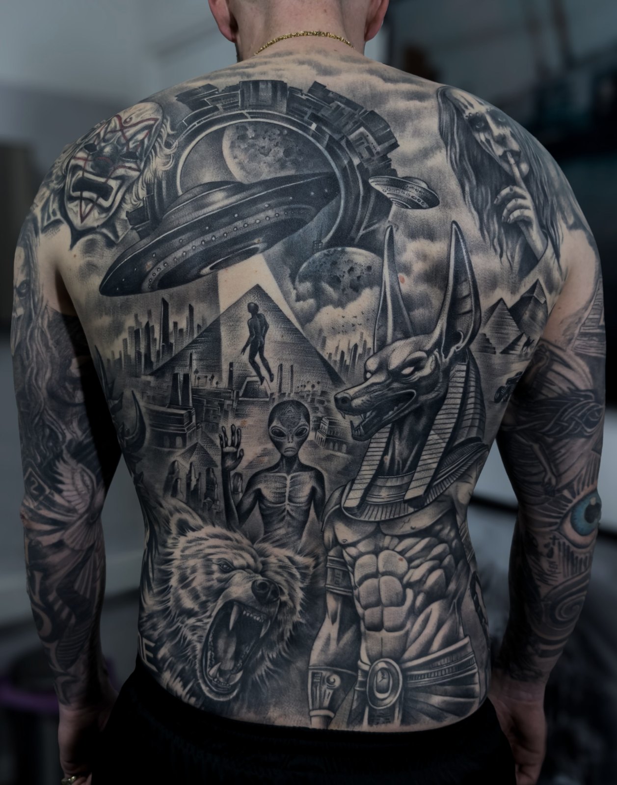 Black and grey back piece by Cipas: Anubis, a bear, an alien and a UFO above the pyramids